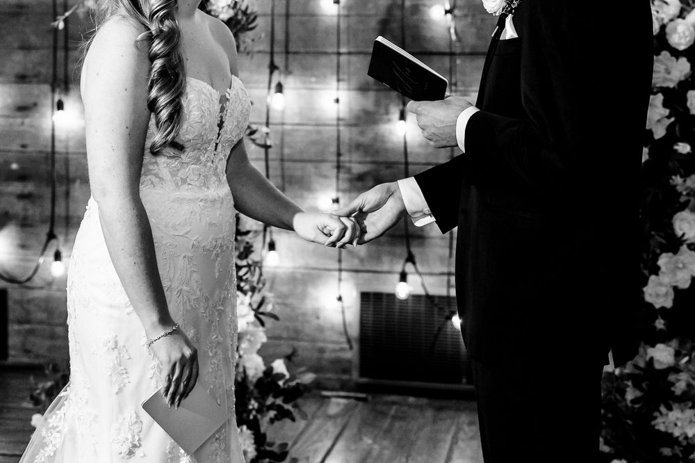 A couple holds hands during their wedding ceremony under twinkling string lights and floral decorations.