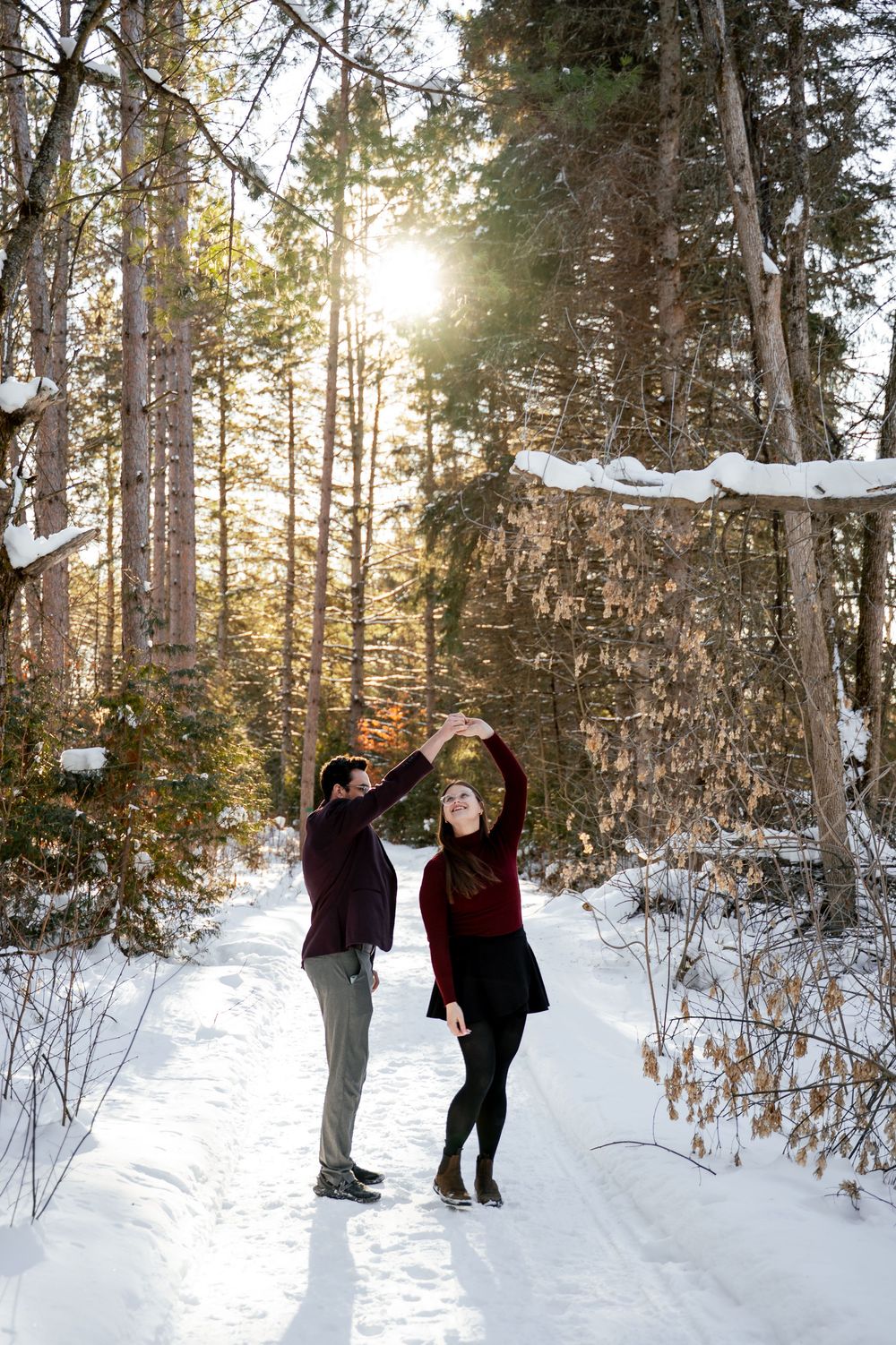 People enjoying a snowy winter forest scene with sunlight filtering through evergreen trees in the background.