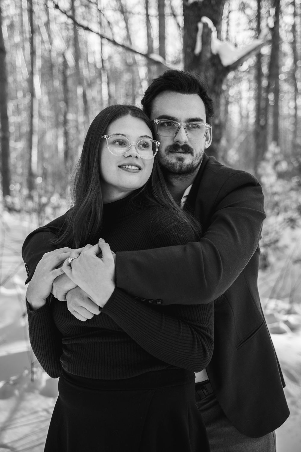 Black and white winter engagement photos showing tender embraces in a snow-covered forest.