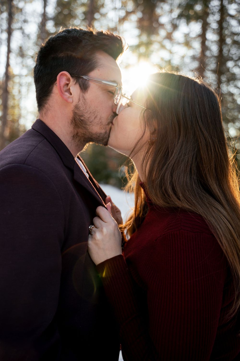 Intimate couple sharing a kiss in the forest with sunlight streaming through the trees.