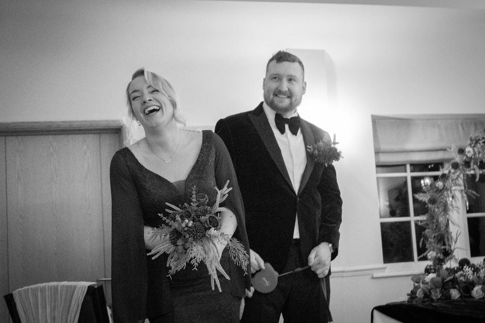 A joyful couple shares a candid moment of laughter during a black and white wedding photoshoot.