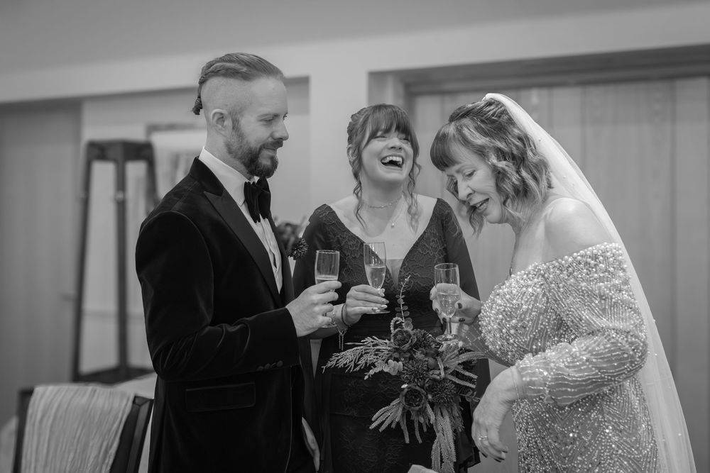 A candid black and white wedding moment showing joyful laughter shared between a couple and their officiant during the ceremony.