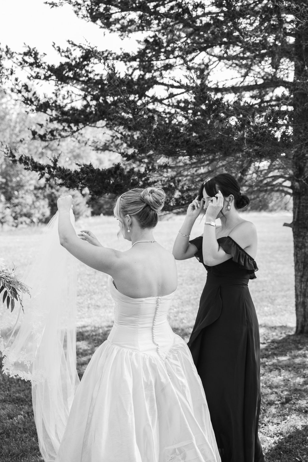 A row of white wedding dresses and a black dress hanging outdoors against a natural backdrop of trees.