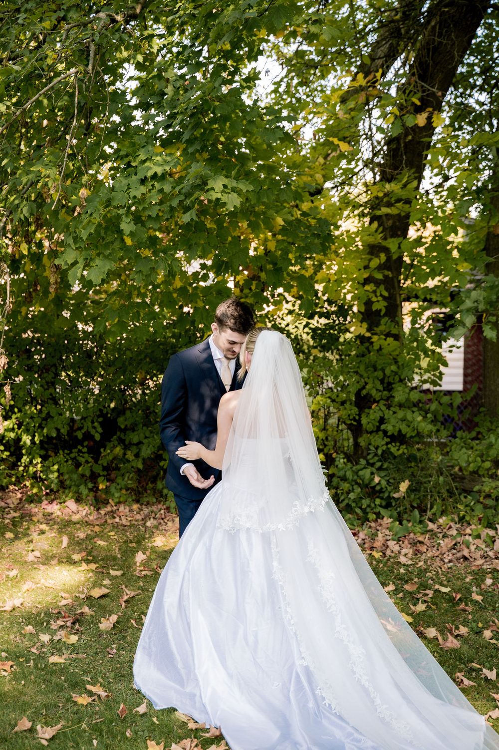 A romantic outdoor wedding photoshoot with a couple in formal attire dancing among autumn trees and fallen leaves.