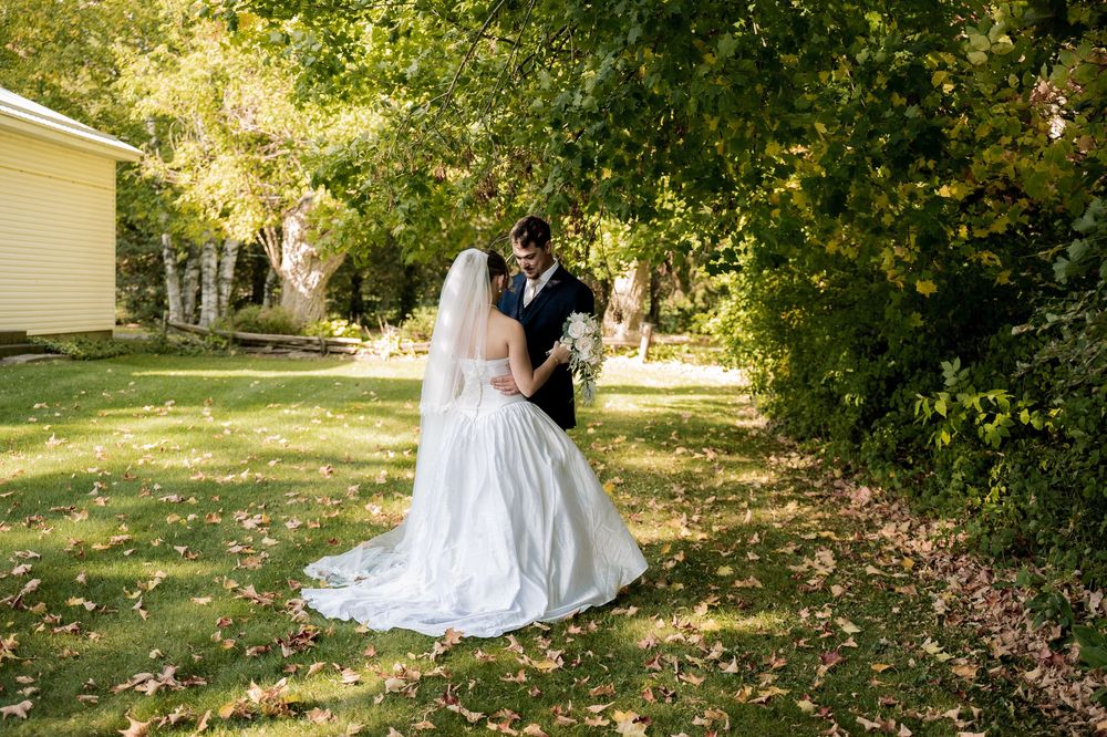 A couple in wedding attire shares an intimate moment together in a sunlit garden setting with lush greenery.