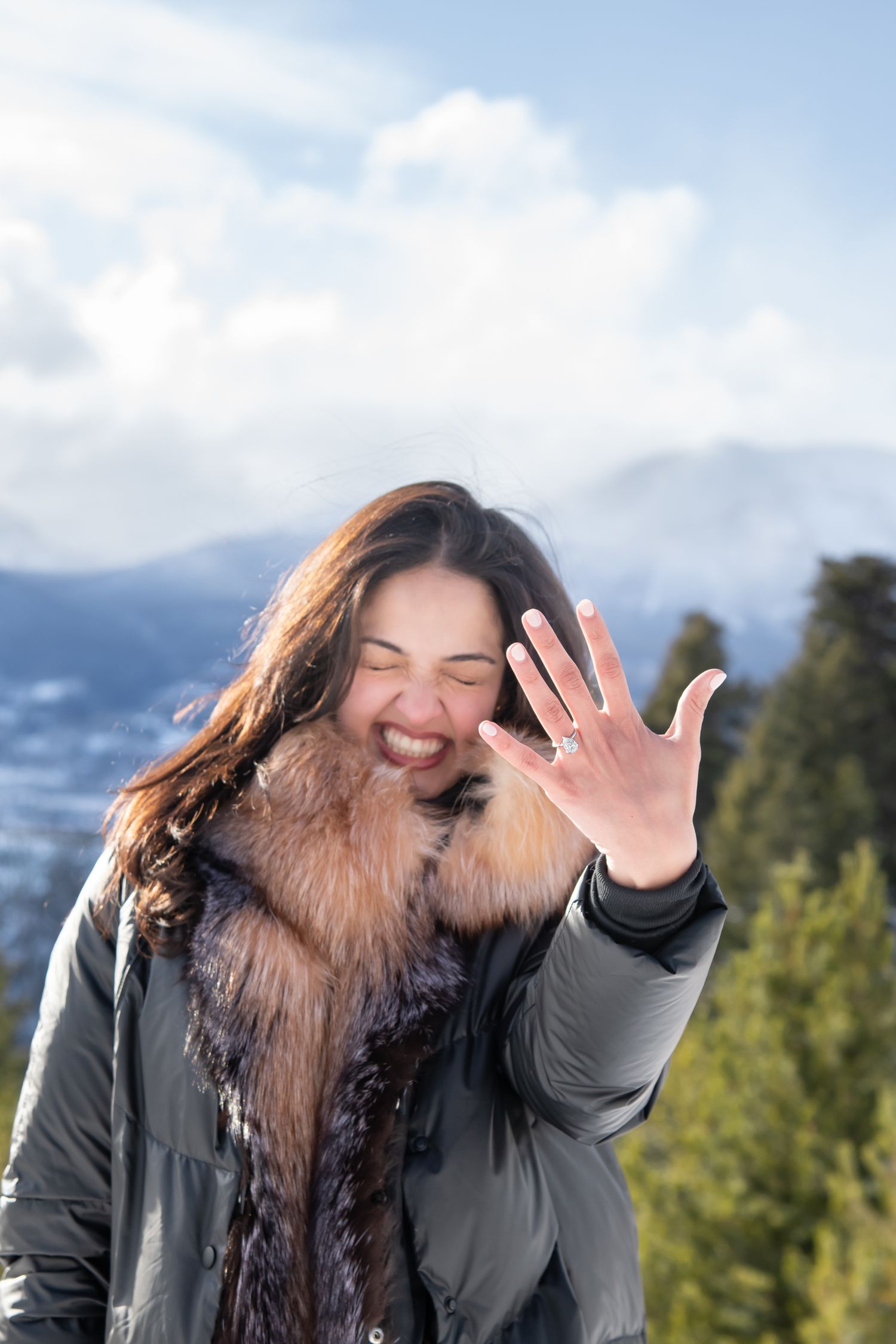 Cute and excited woman shows off her new engagement ring while wearing cute winter fashions for proposal at Sapphire Point