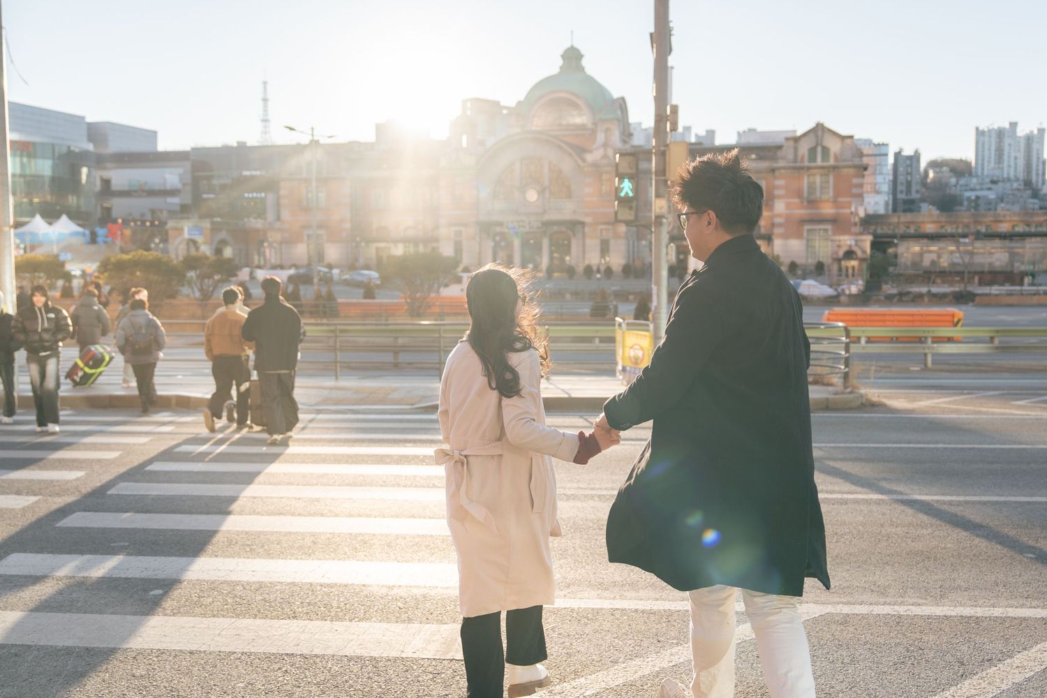 People walking through a city square at sunset with long shadows cast on the pavement.
