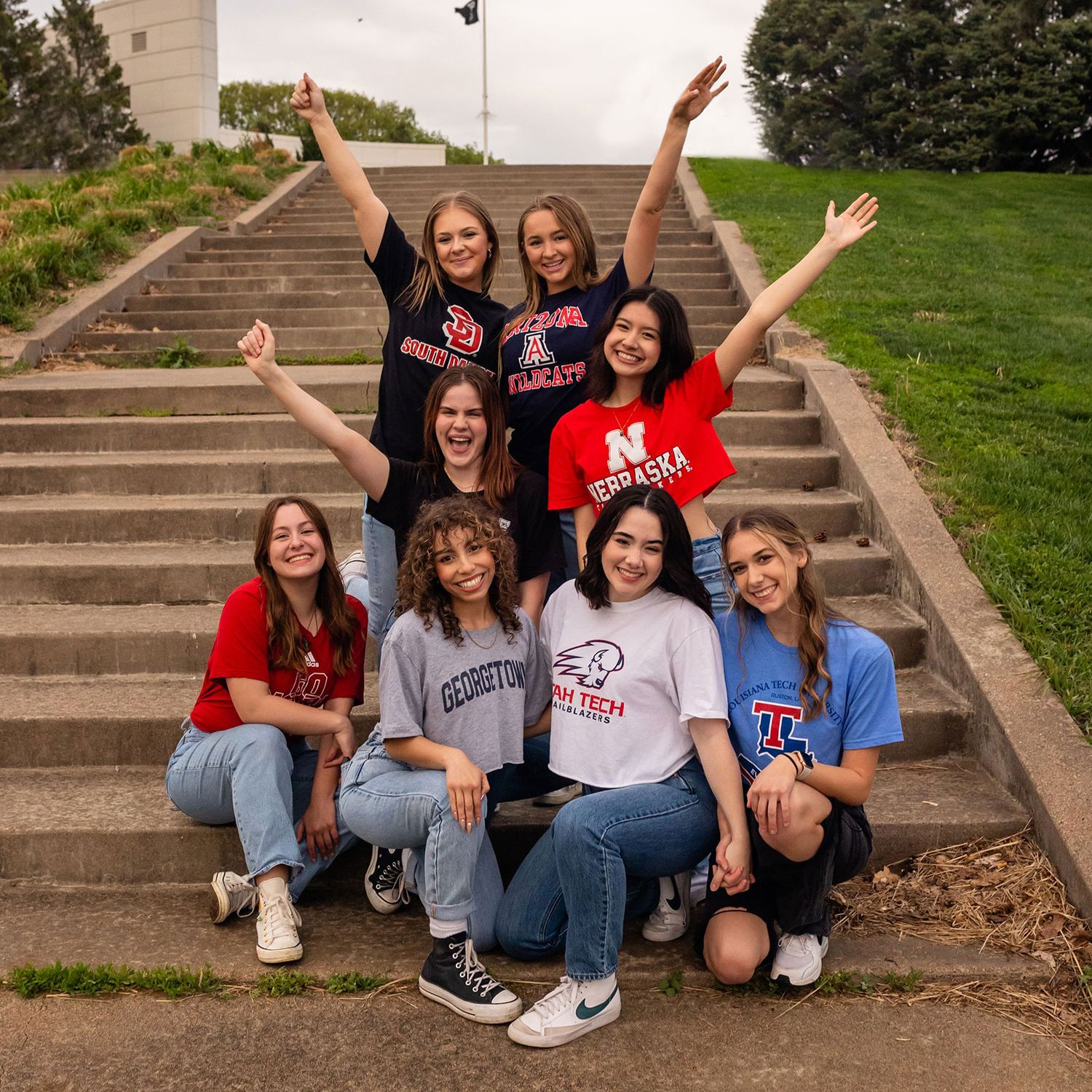 A group of friends sitting on concrete step wearing university apparel and casual clothing at Memorial Park in Omaha, NE for graduation