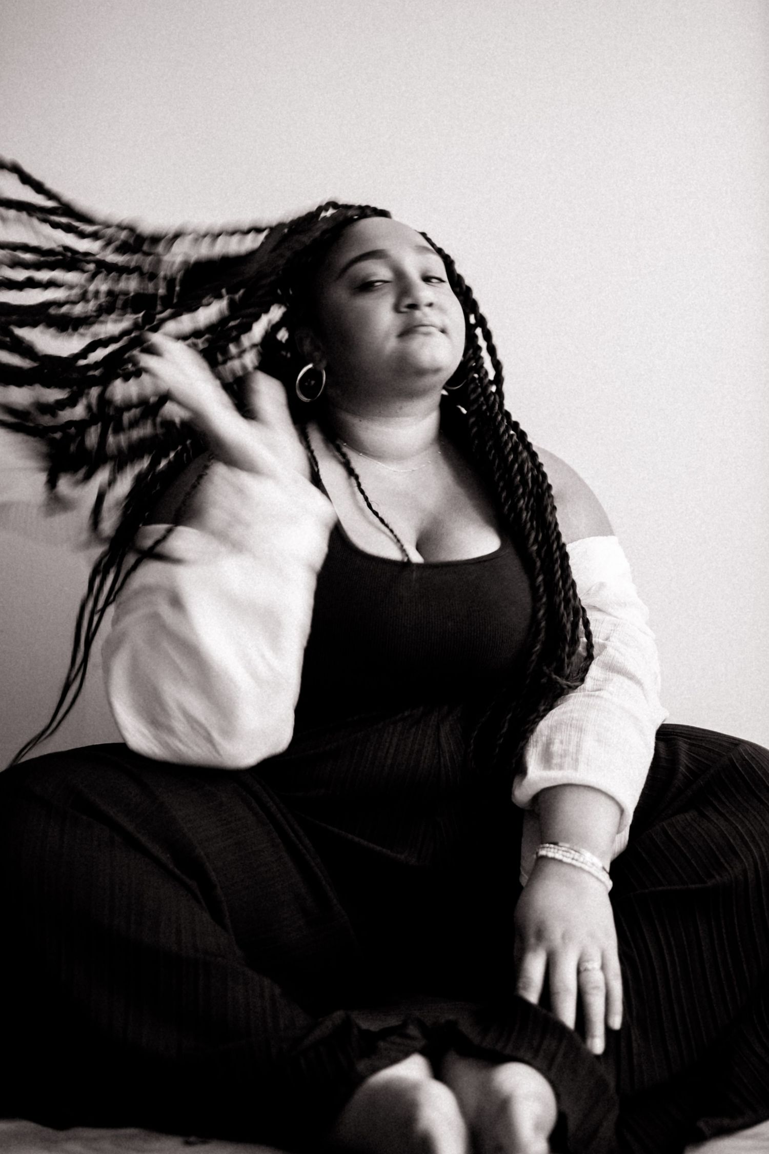A woman in black and white attire flips her braided hair while posing confidently in a studio setting.
