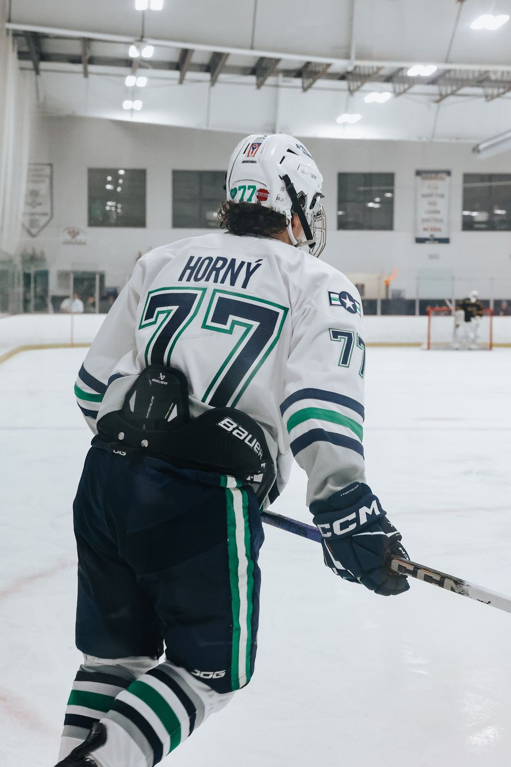 Hockey player in black and white uniform with number 77 skates on indoor ice rink during game.