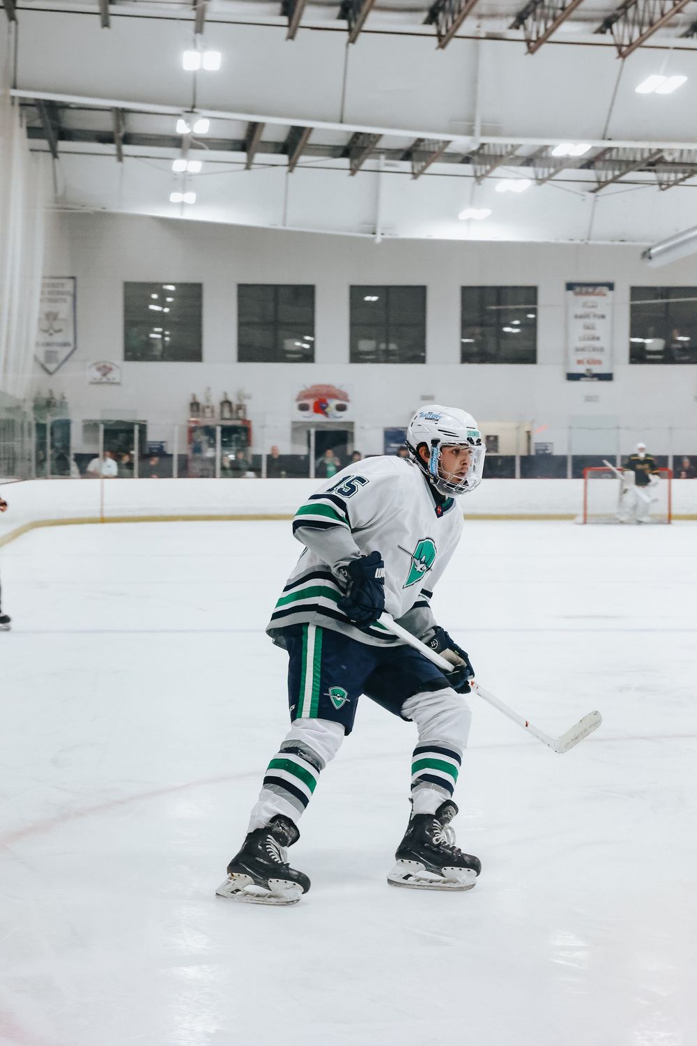 Hockey player in white and green uniform skating on ice during practice session.