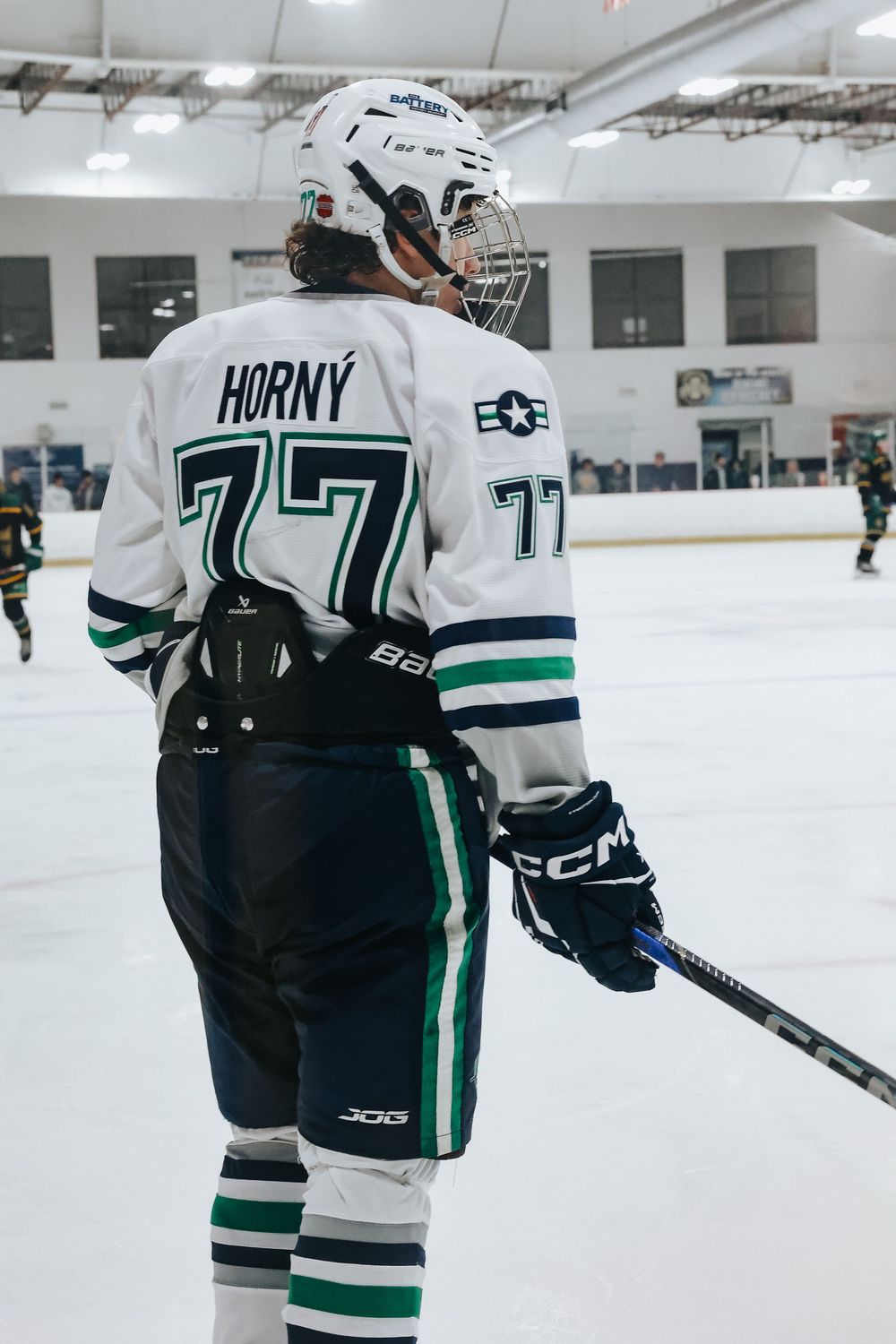 Hockey player in white and green uniform skating on ice rink during practice session.