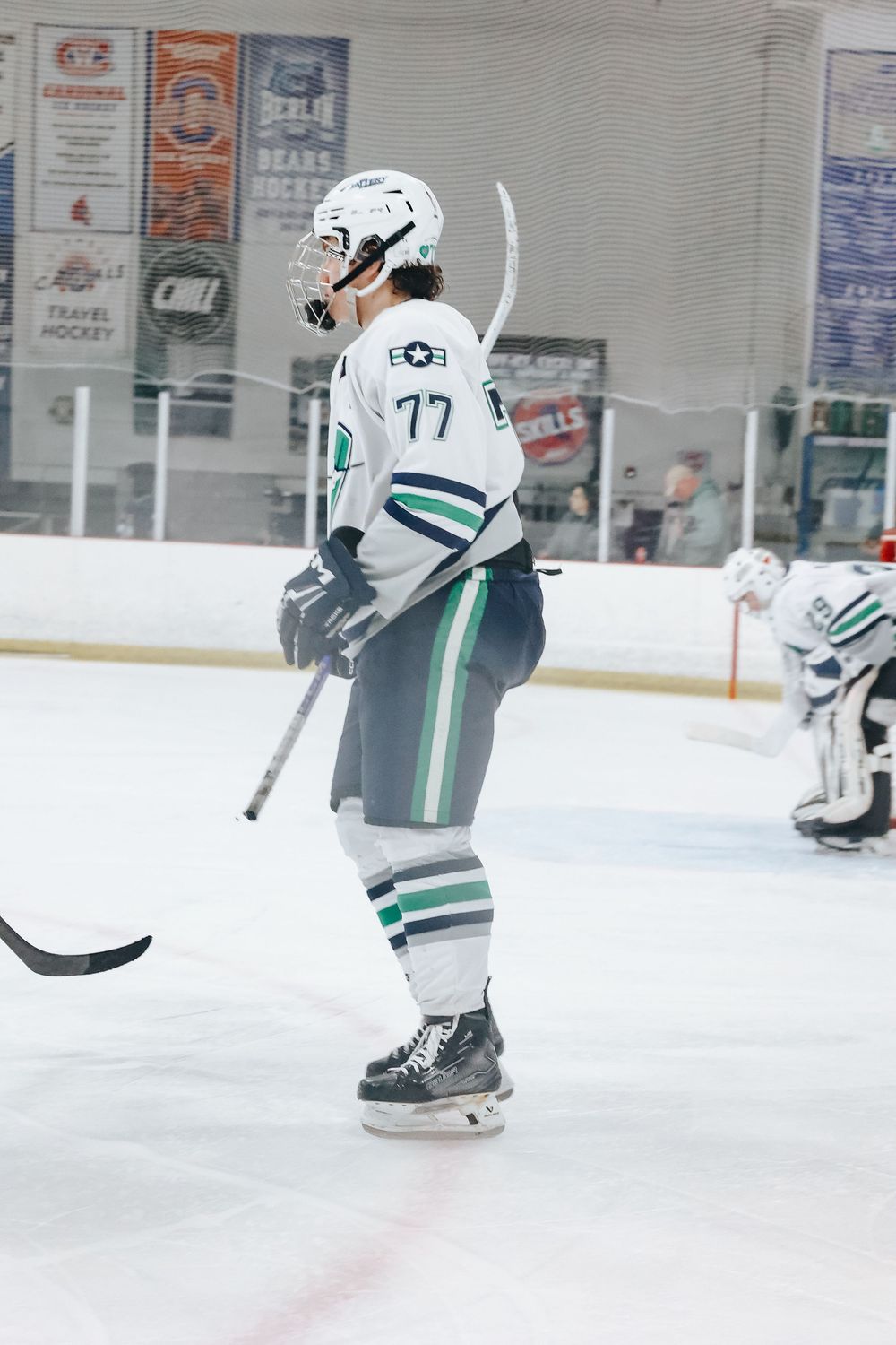 Hockey player gliding on ice in white and green jersey with hockey stick in hand.