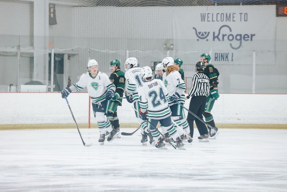 Ice hockey players in white and green jerseys compete during a game at a Kroger-sponsored rink.