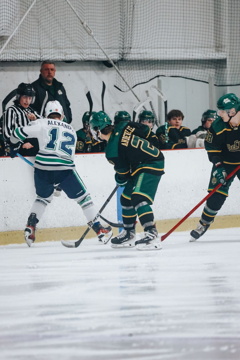 Youth hockey players in green and white uniforms battle for position during game.
