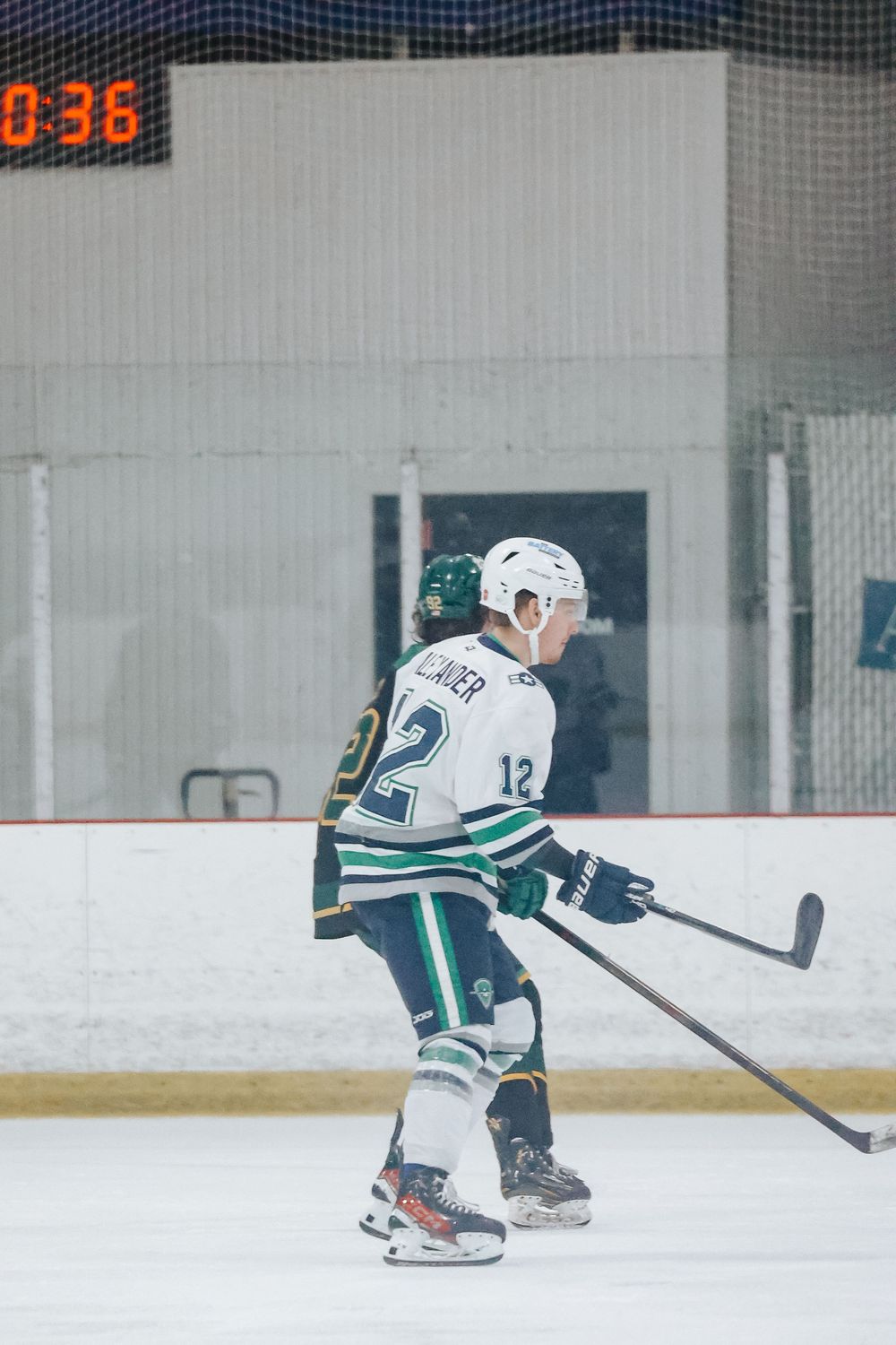 Hockey players in white uniforms practicing drills on indoor ice rink with scoreboard visible.