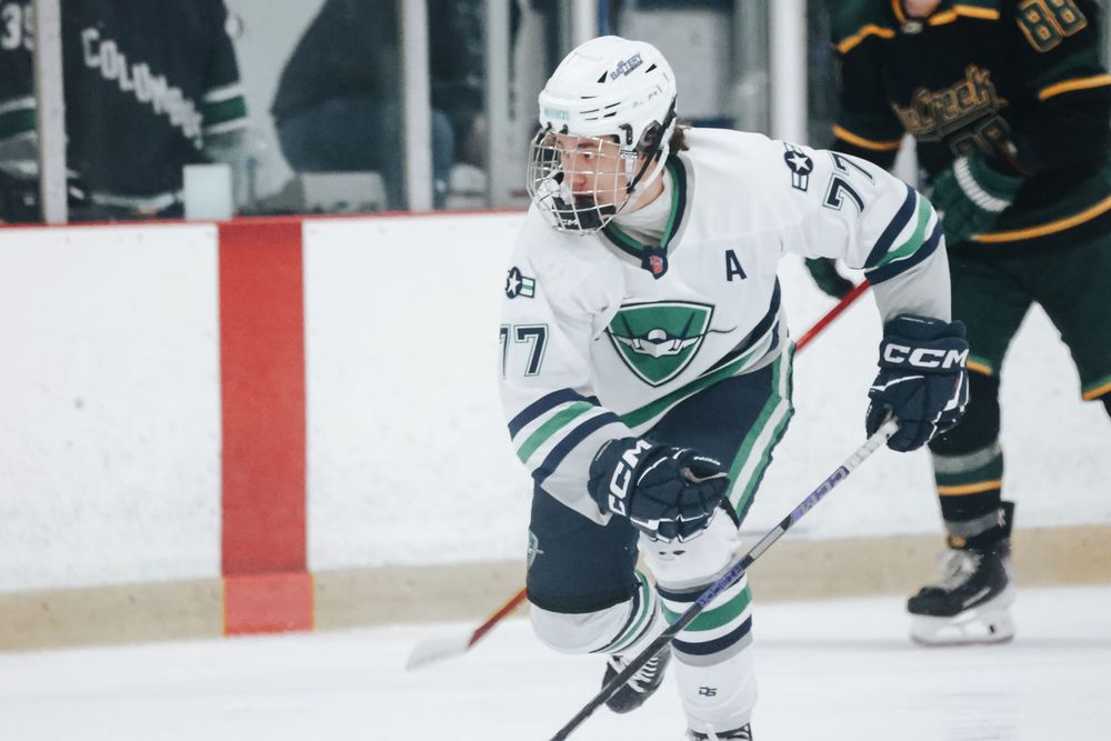 Ice hockey player in white jersey skates on ice during competitive match with opposing team in dark uniforms.
