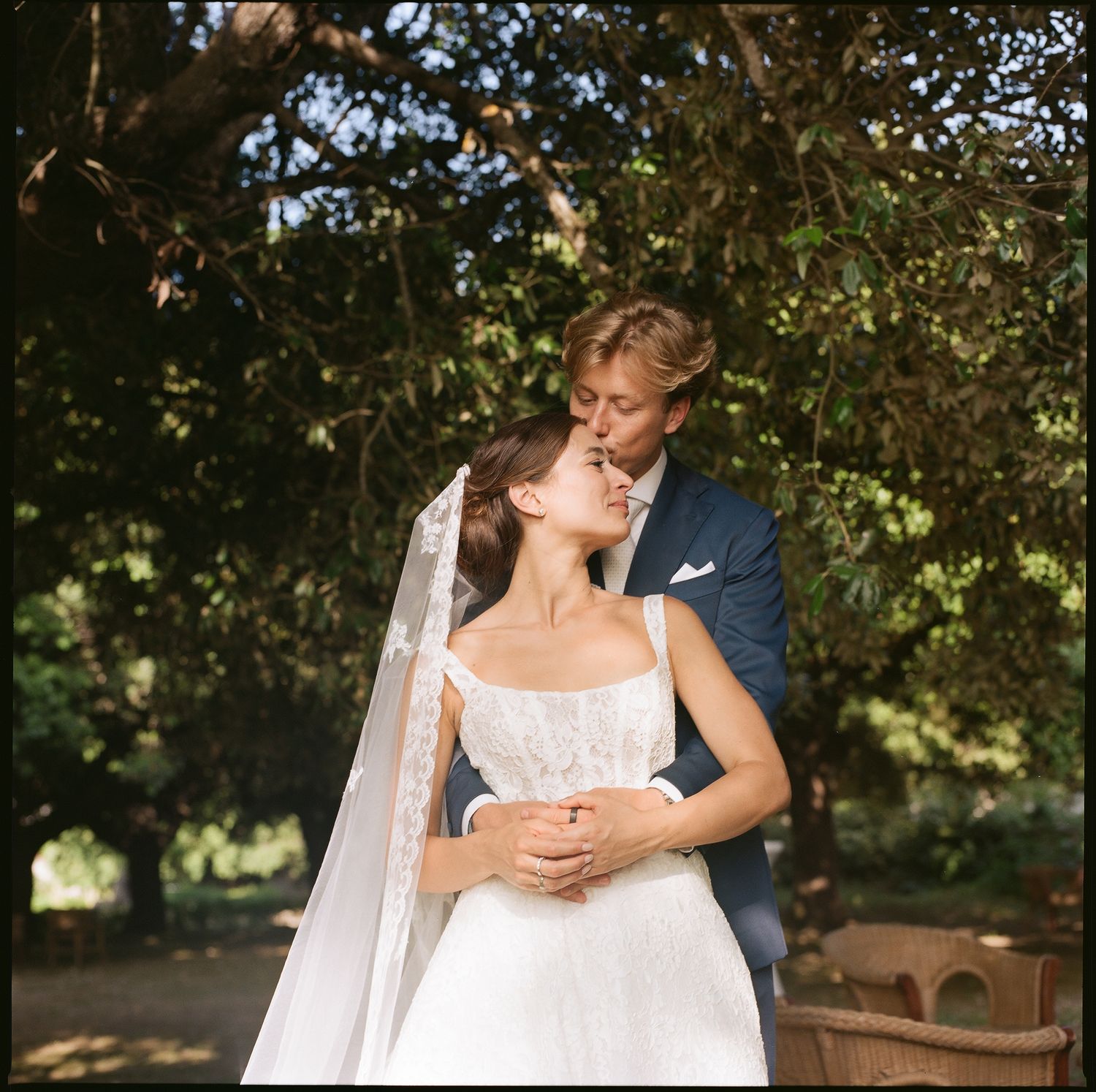 A romantic wedding couple stands beneath a tree canopy in silhouette during a golden sunset photoshoot.