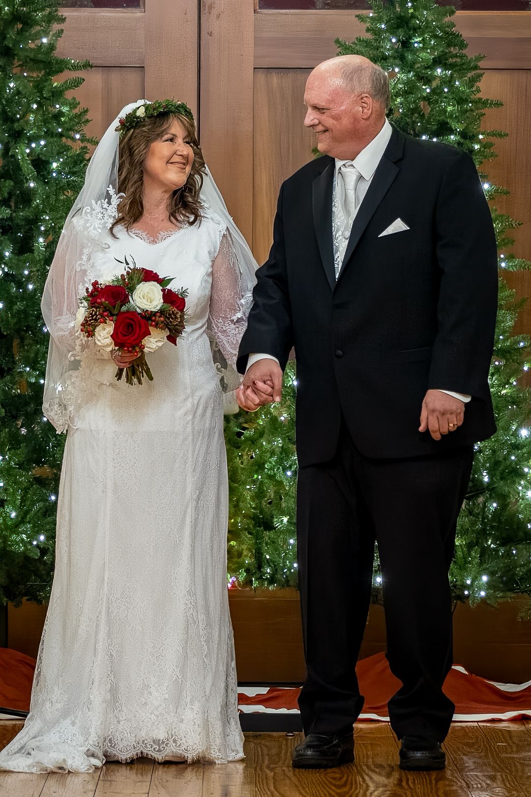 Frederick Maryland Wedding Photographer  Newlyweds share a joyful moment in front of decorated Christmas trees at their winter wedding
