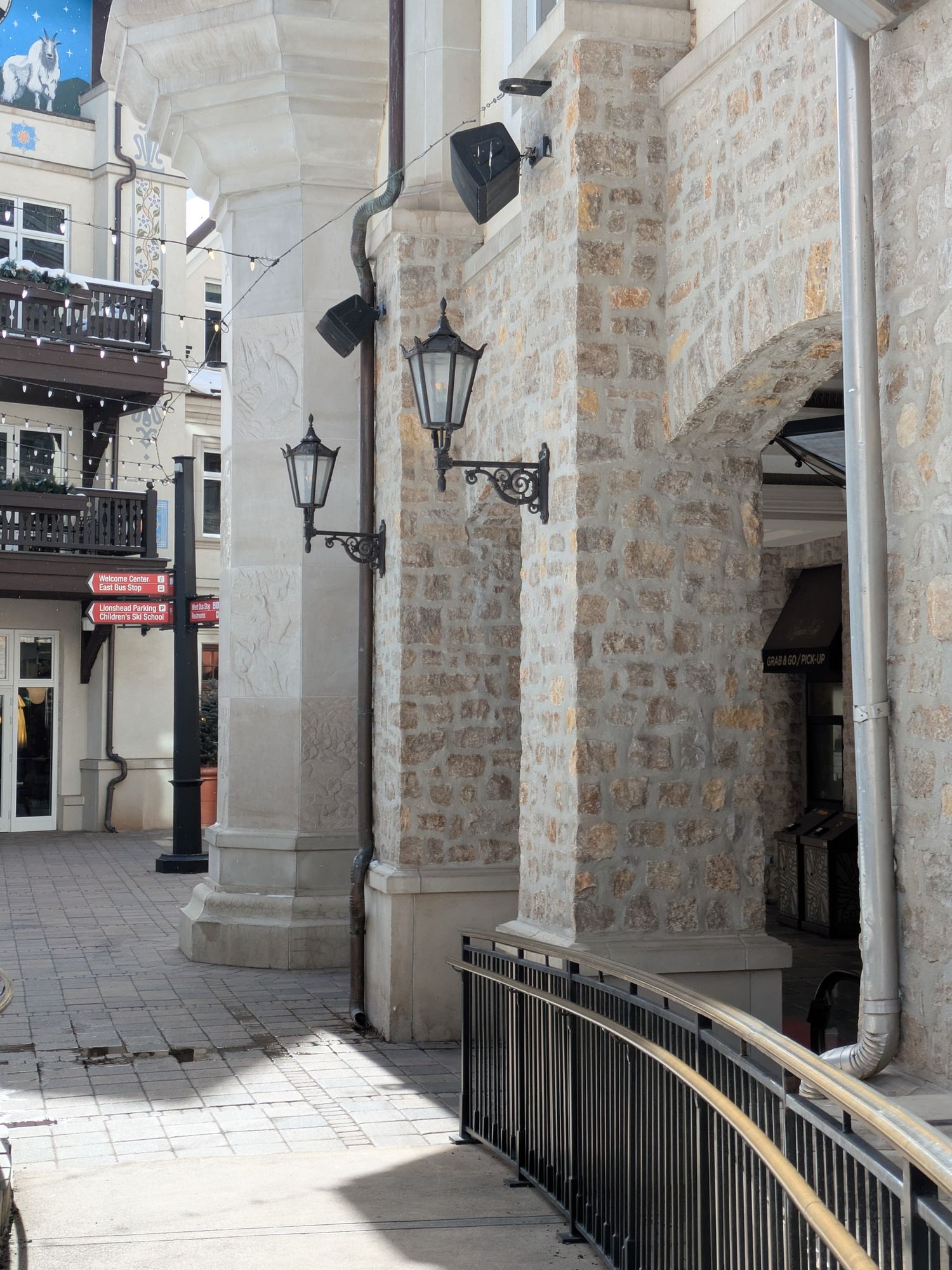 Stone archway with black lamp posts and railings along a curved walkway in a historic building exterior.