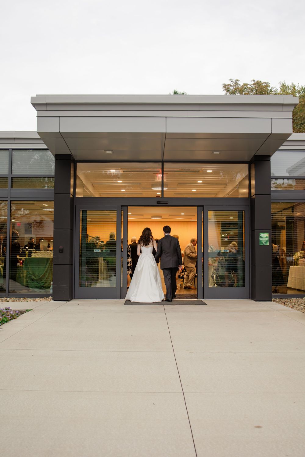 Modern building entrance with glass doors and concrete facade illuminated by interior lighting at dusk.