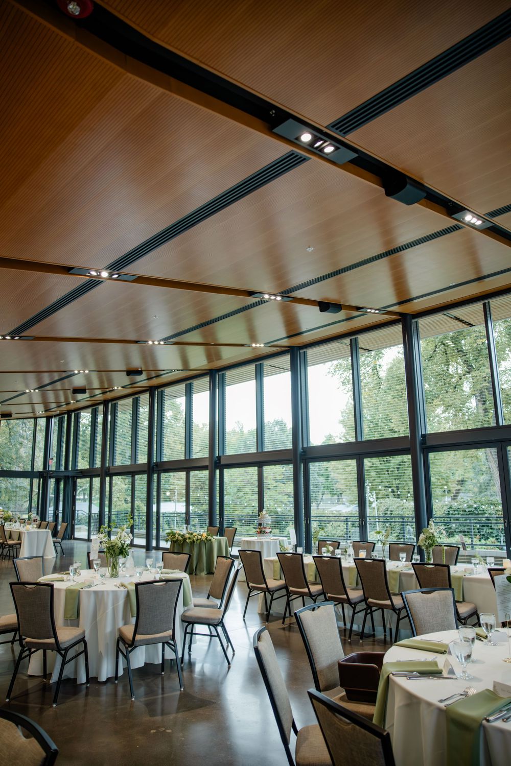 Modern restaurant dining room with floor-to-ceiling windows, white tablecloths and elegant decor overlooking a scenic outdoor view.