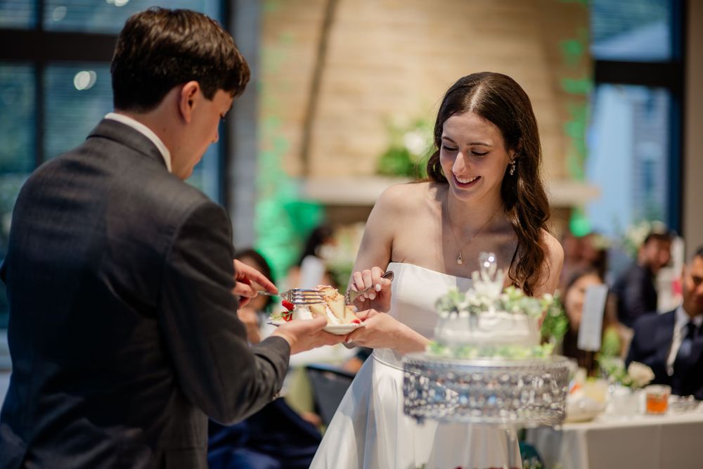 A couple cuts into their elegant three-tiered white wedding cake during a reception celebration.