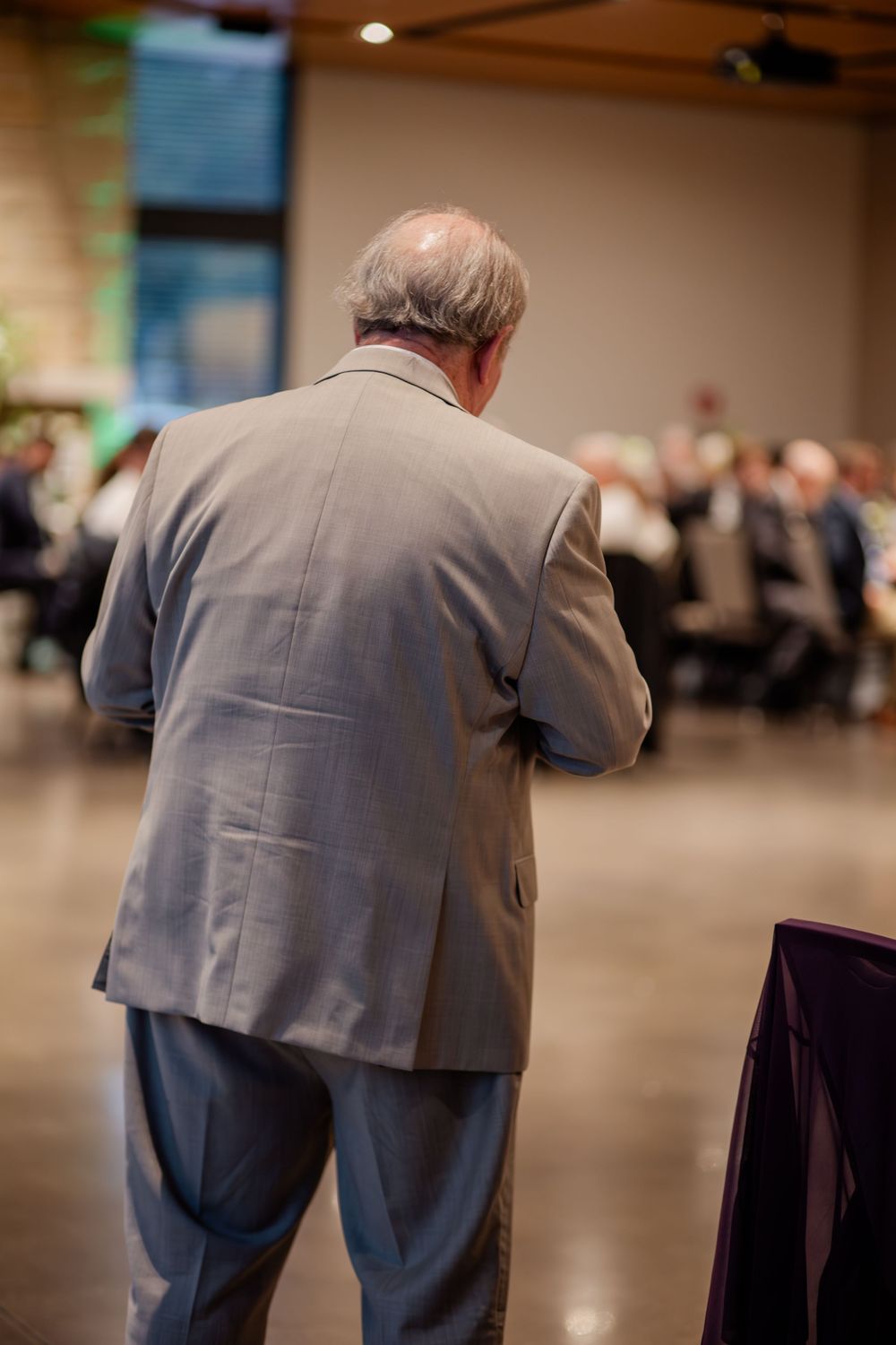 A person in a grey suit jacket bending over chairs at what appears to be an event venue.