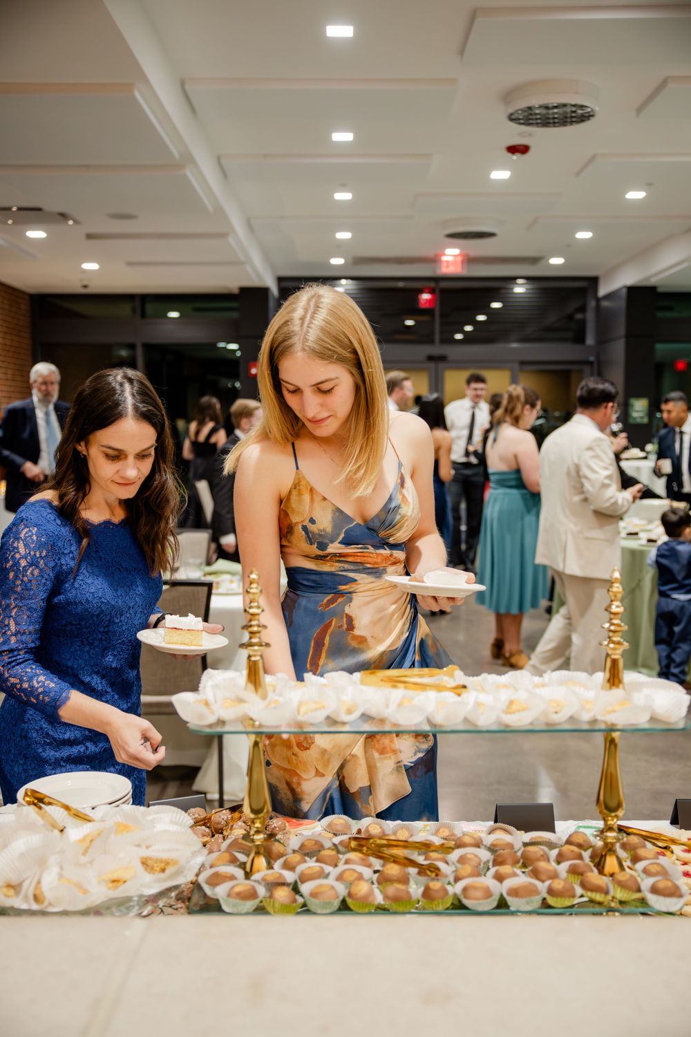 People in formal attire gather around a buffet table selecting food and appetizers at an elegant event.