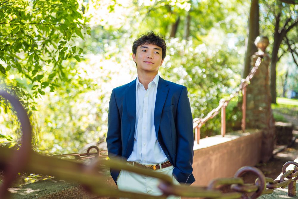 Student in business attire poses outdoors against natural greenery backdrop. Dallas Graduate Portraits by Eric Aaberg Photography in DFW.