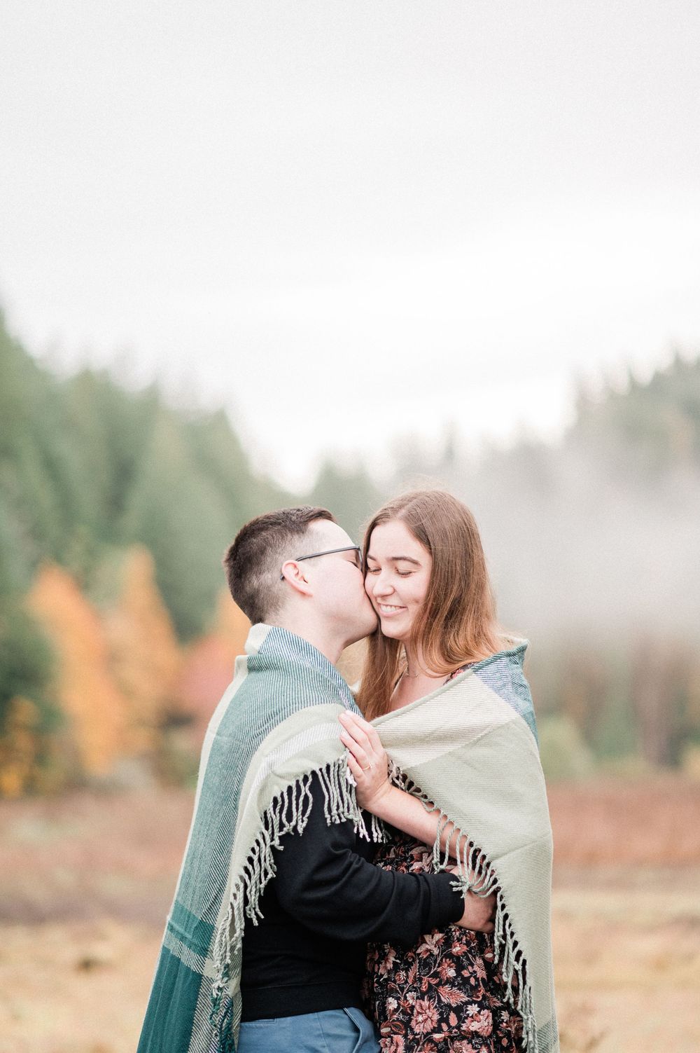 A couple wrapped in a cozy blanket share romantic moments in a misty autumn field.