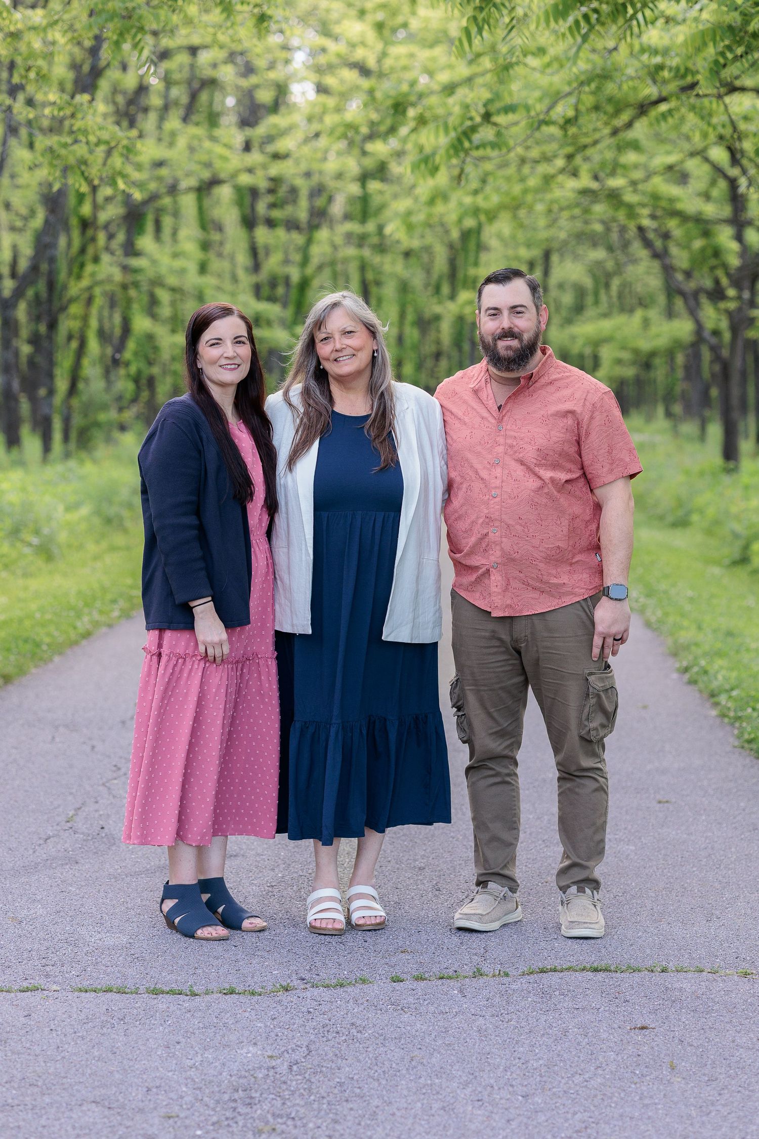 Family group portrait on paved path with lush green forest background.