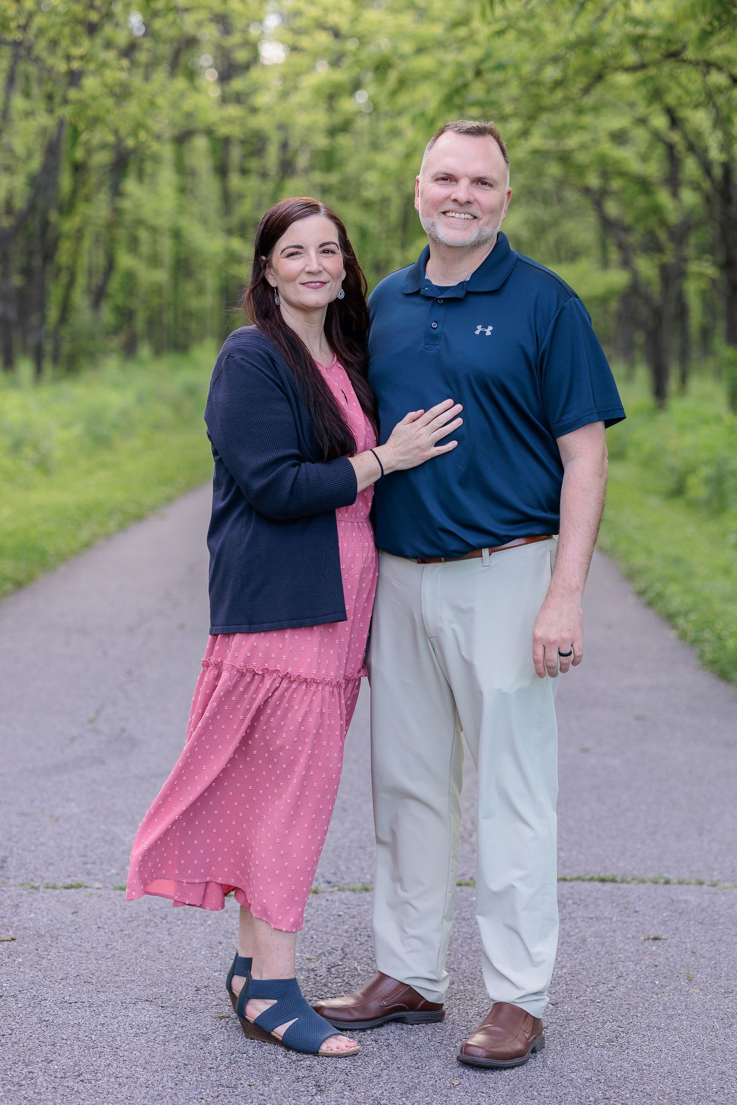 A couple poses together on a tree-lined path, wearing coordinated blue and pink outfits.