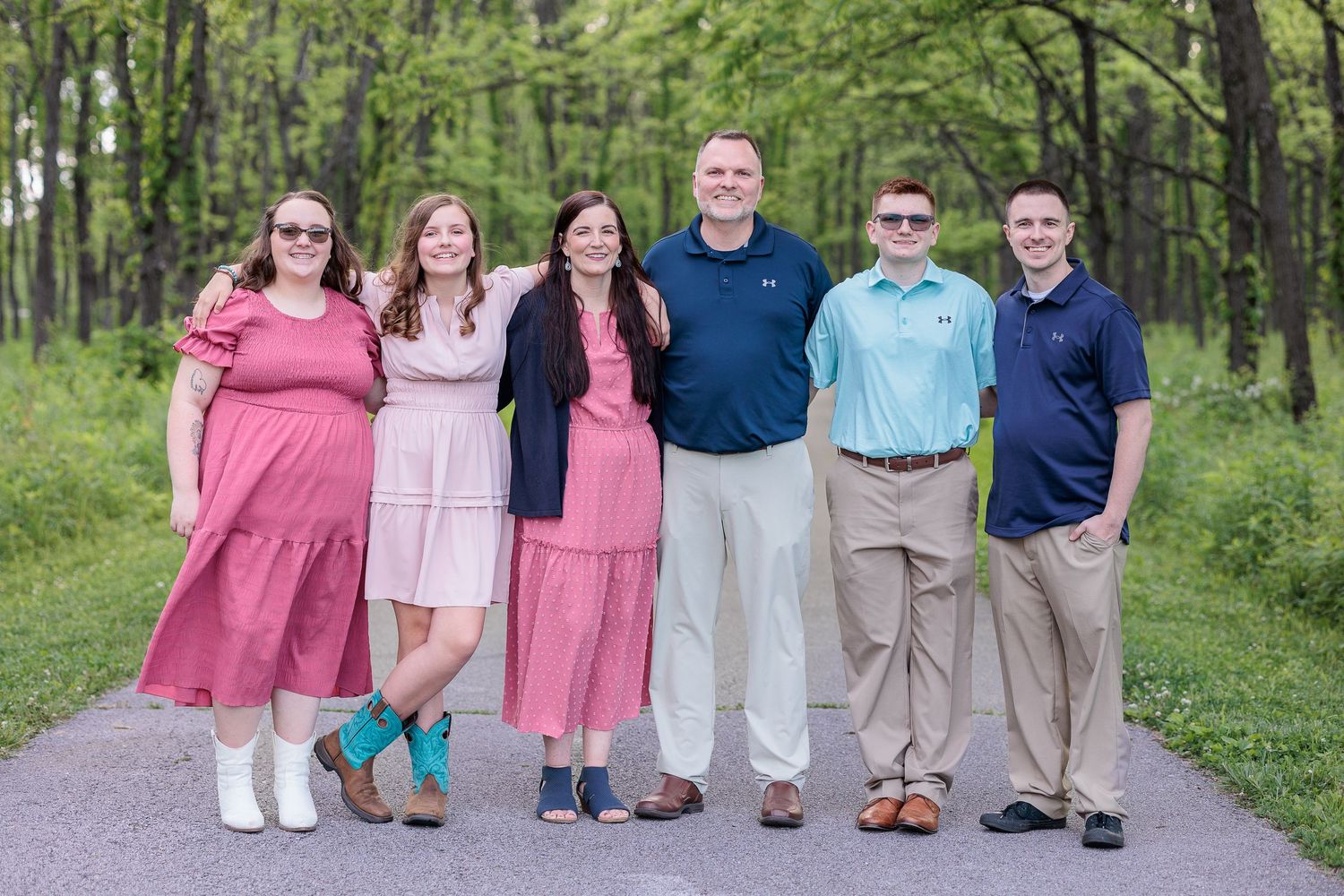 A family in coordinating pink and blue outfits stand together on a wooded path for a photo at Fort Harrison State Park.
