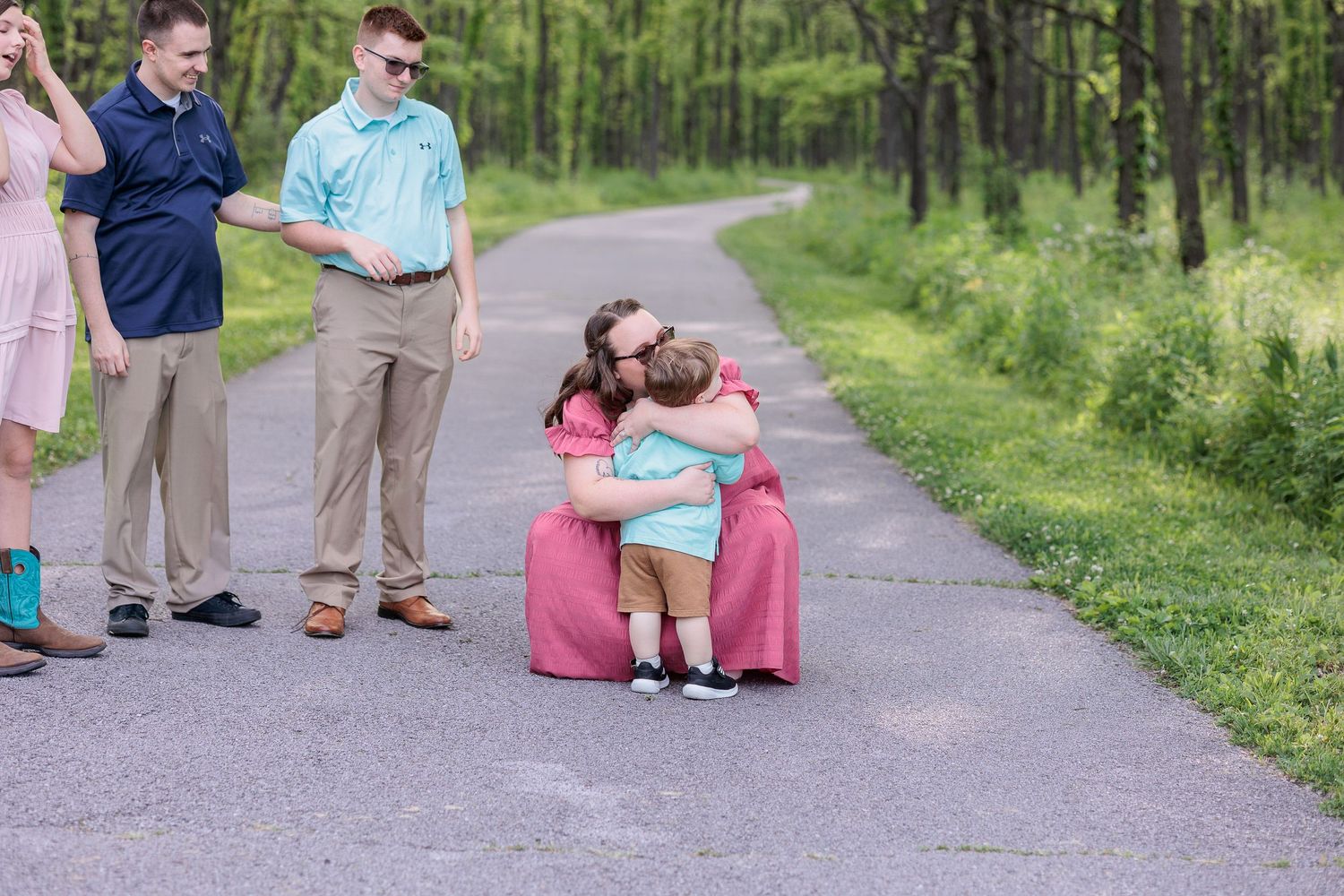 Mother and toddler share an emotional embrace along a tree-lined path.