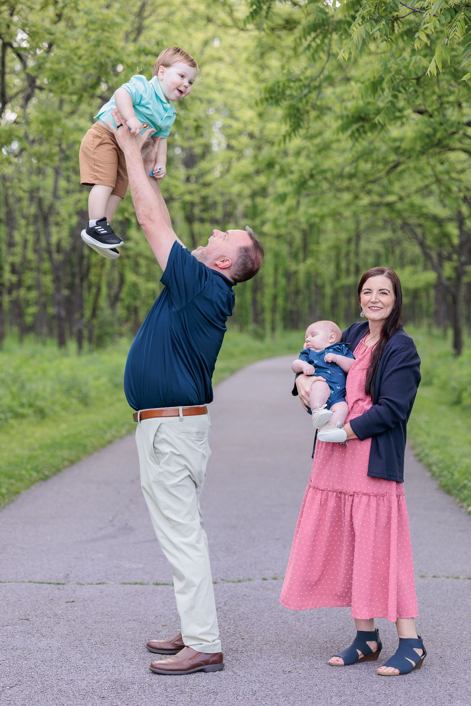A family shares playful moments together on a tree-lined path during a spring photo session.