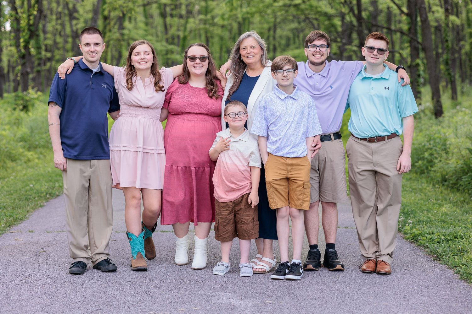 A group portrait of family members in coordinated outfits standing on a wooded path.