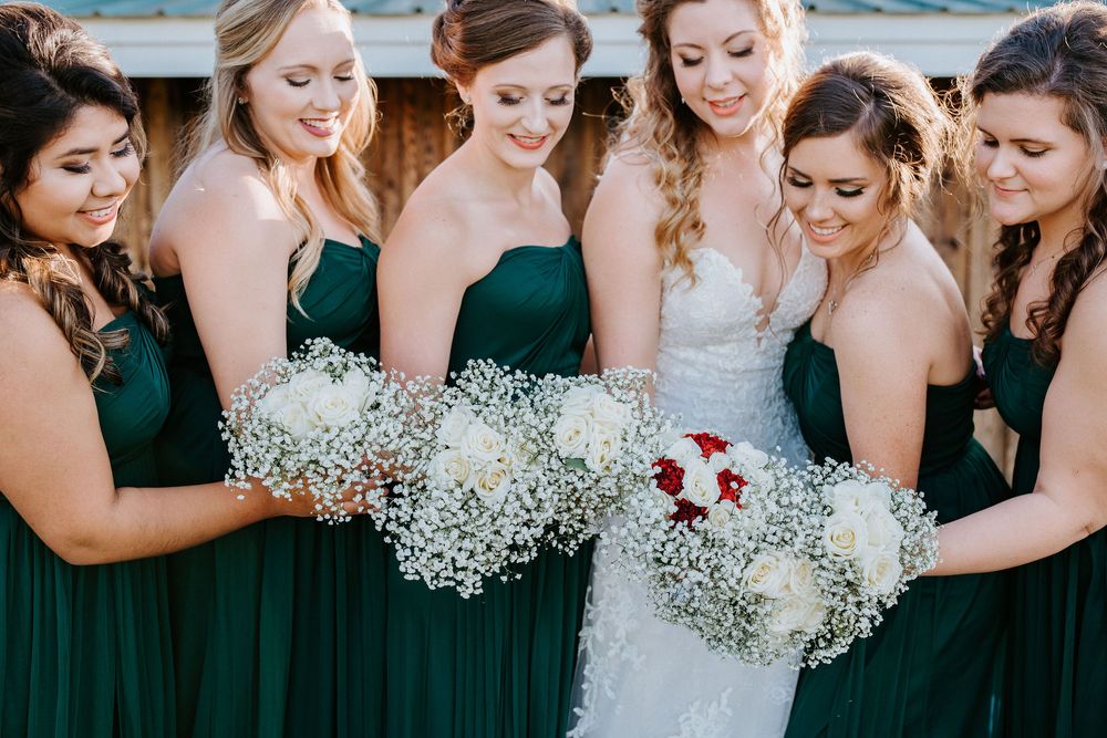 Wedding party in dark green dresses and white floral bouquets standing together outdoors.