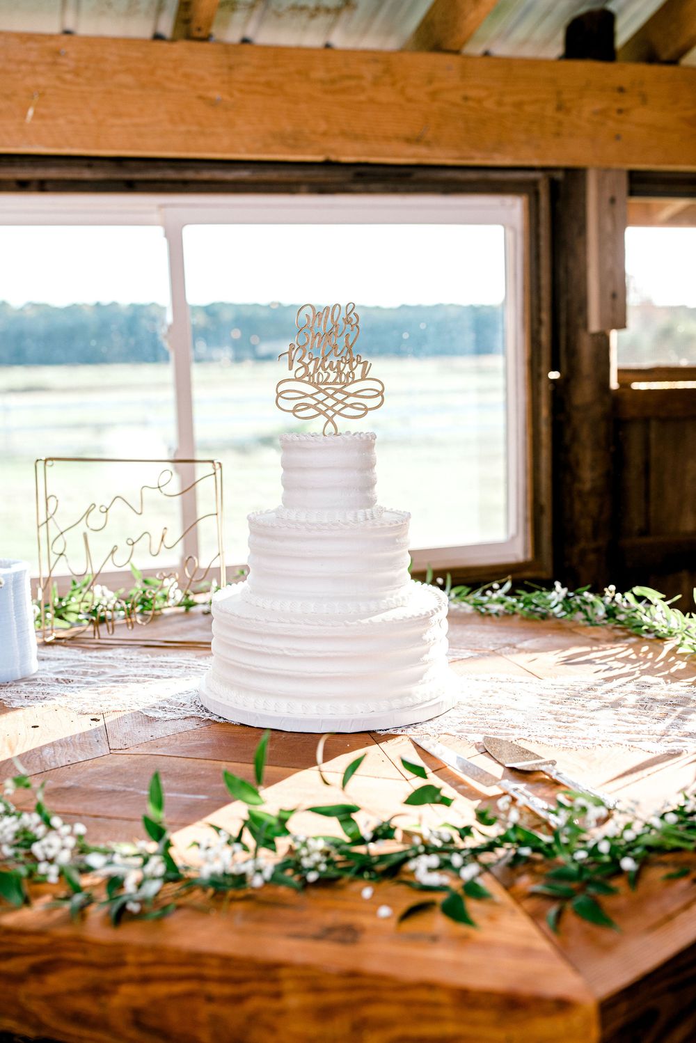 White wedding cake with floral decorations displayed on rustic wooden table with greenery garland.