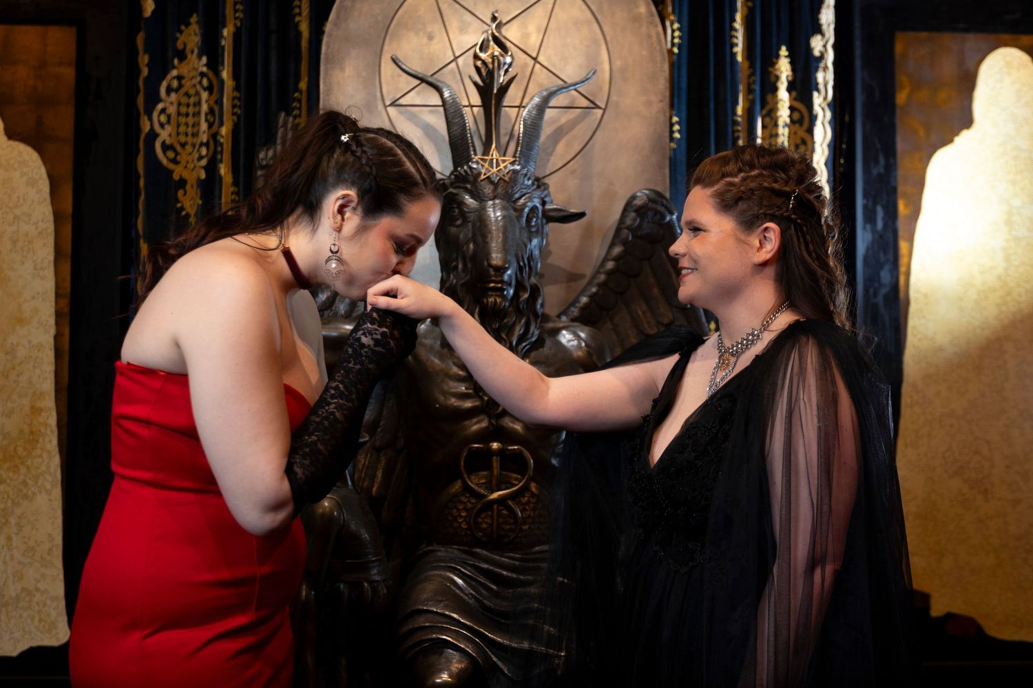 Two people in formal attire share an intimate moment in a dimly lit room with ornate decor.