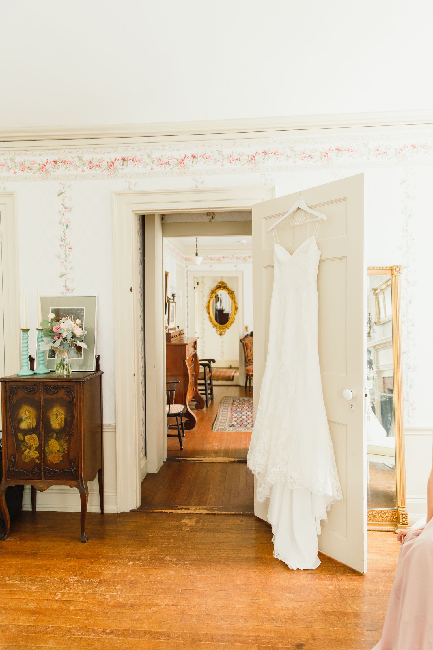 An elegant white wedding dress hanging in a vintage-style room with hardwood floors.