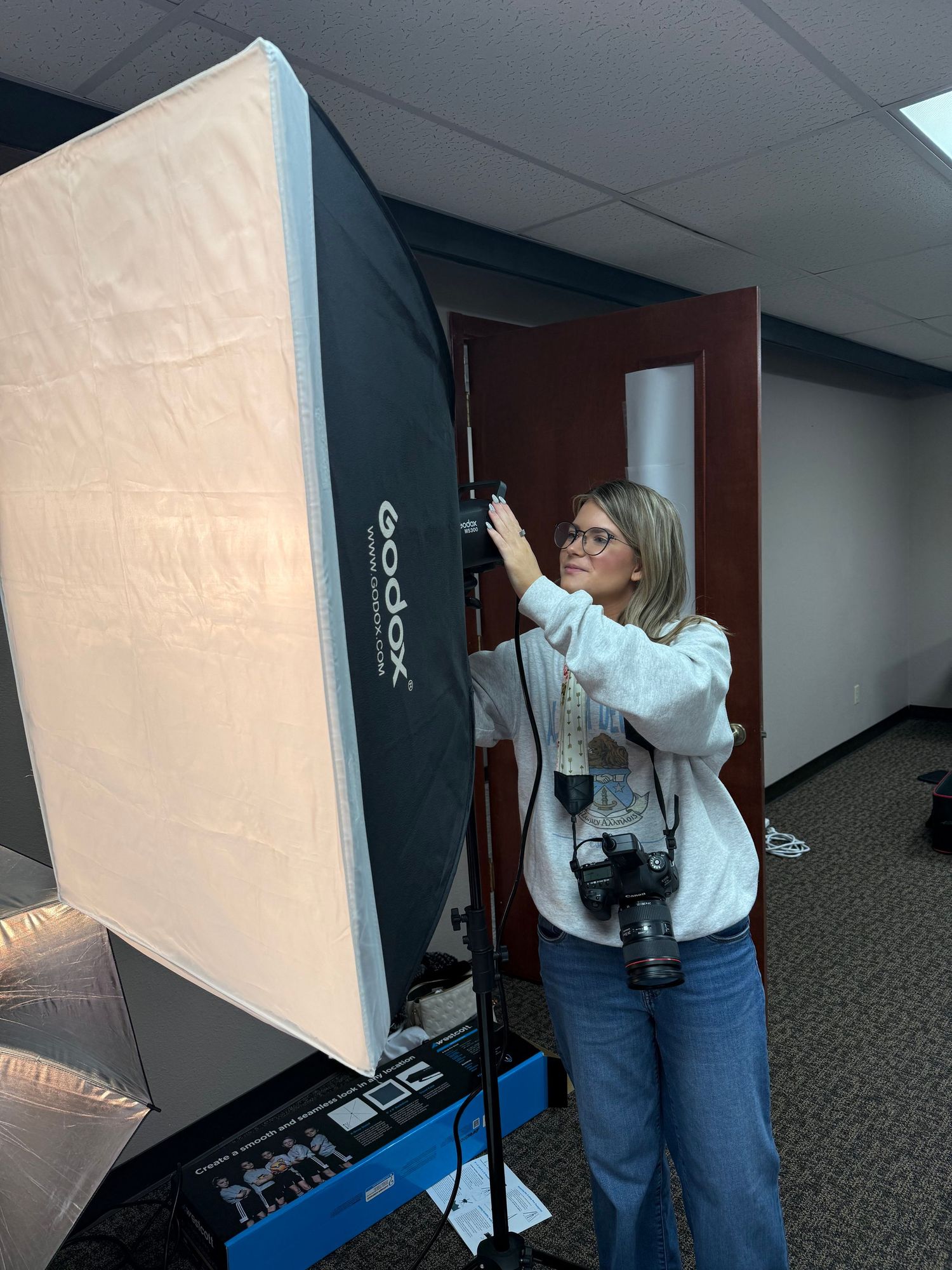 A person in a white shirt and jeans adjusts a white photography backdrop in an office hallway.
