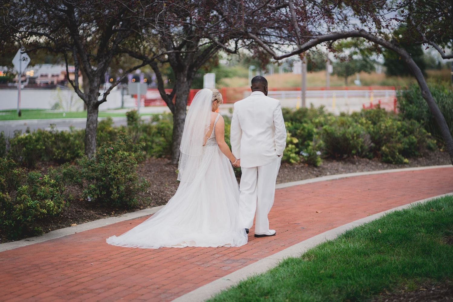 Elegant couple strolling down a winding brick path surrounded by lush greenery.