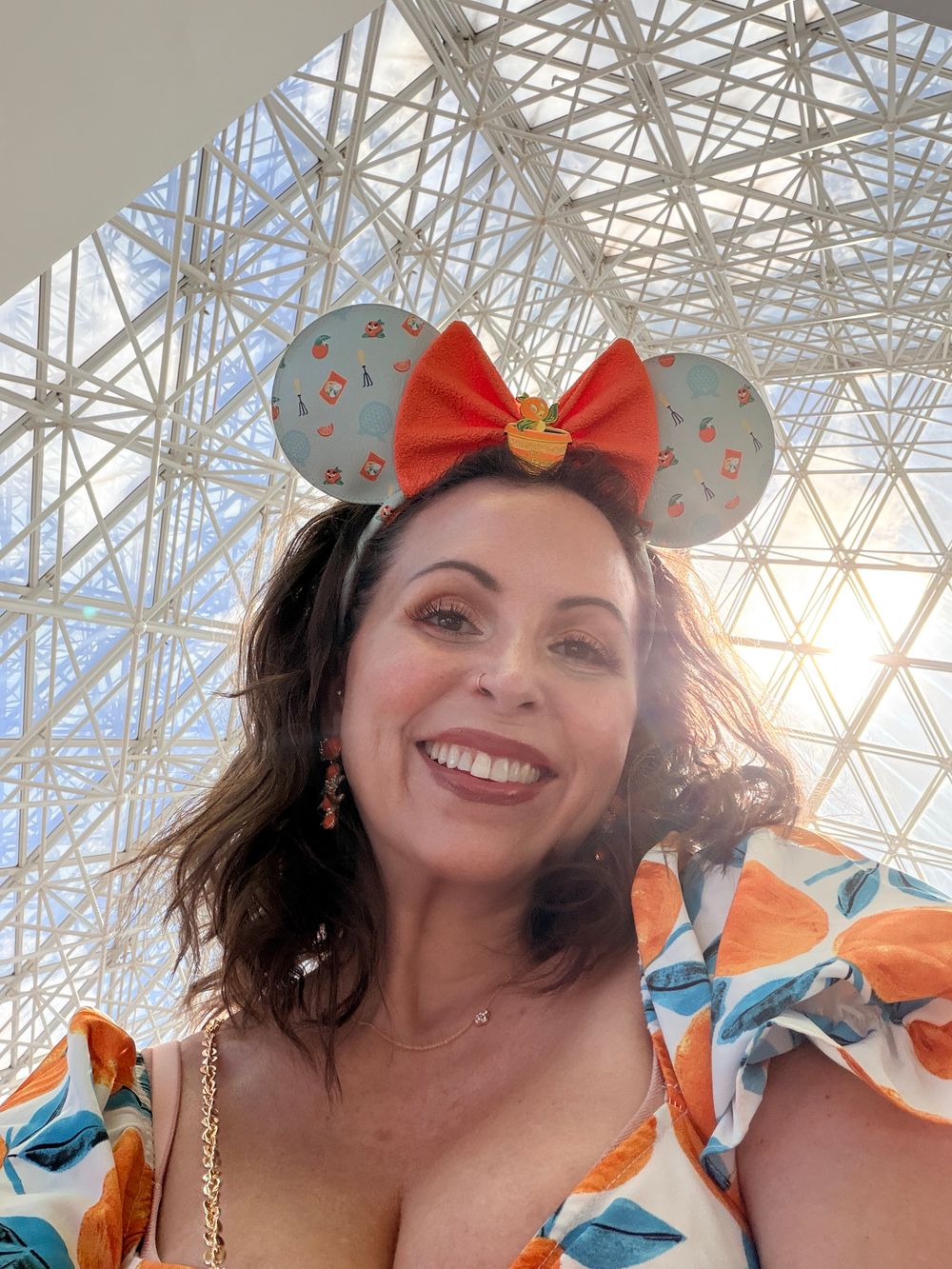 A person wearing a red bow and Minnie Mouse ears poses in front of a geometric domed structure.