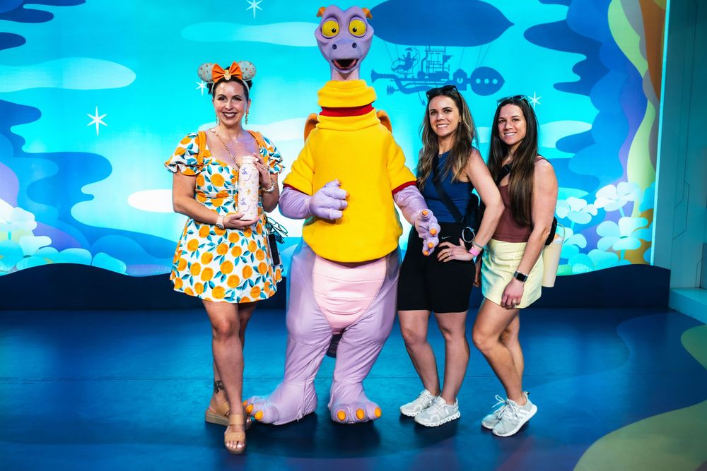 A group poses in colorful outfits against a bright blue background at what appears to be an entertainment venue.