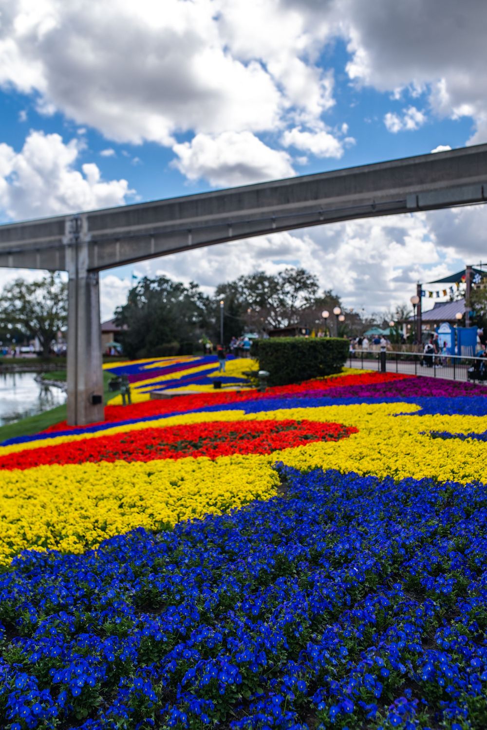 Vibrant display of red, yellow and blue flowers blooming under an elevated monorail track at Walt Disney World.