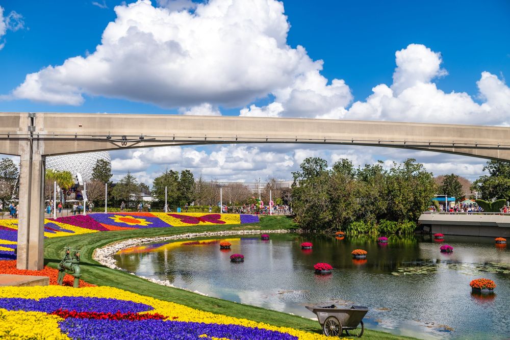Colorful flower gardens and a monorail track surround a peaceful lake at Walt Disney World's EPCOT theme park.