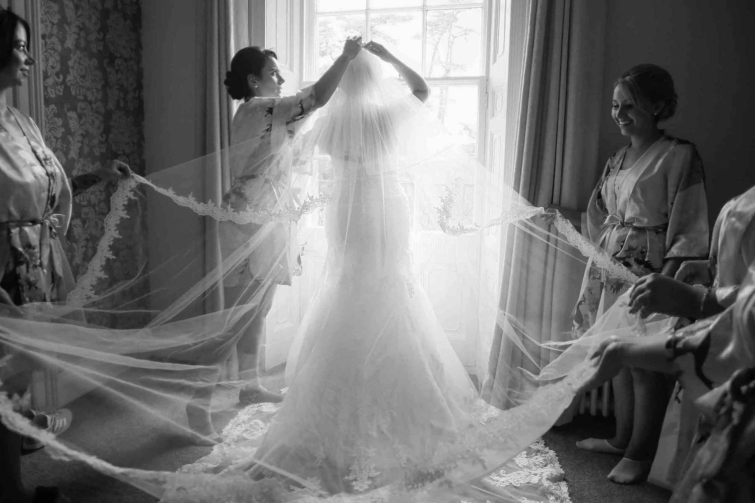 A series of black and white photos showing a wedding dress veil being adjusted near a window in soft natural light.