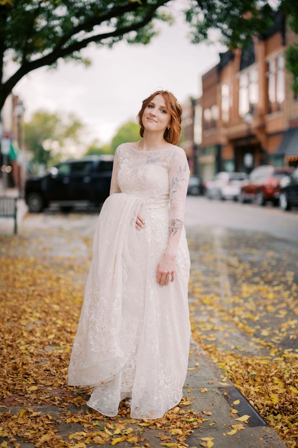 Long-sleeved vintage lace wedding dress photographed on a fall day with golden leaves scattered on city sidewalk.