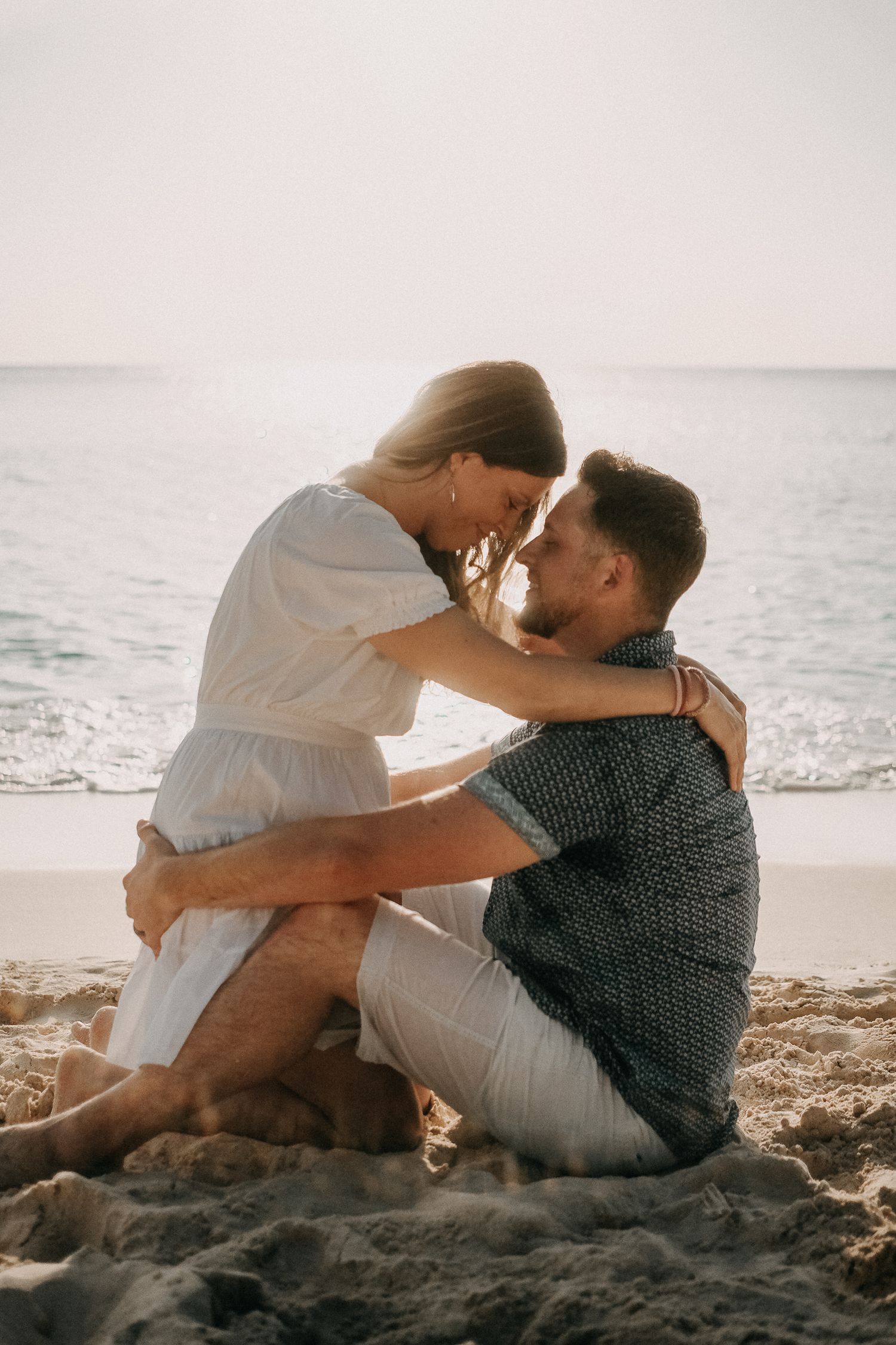Romantic couple sitting together on rocky beach shore at sunset.